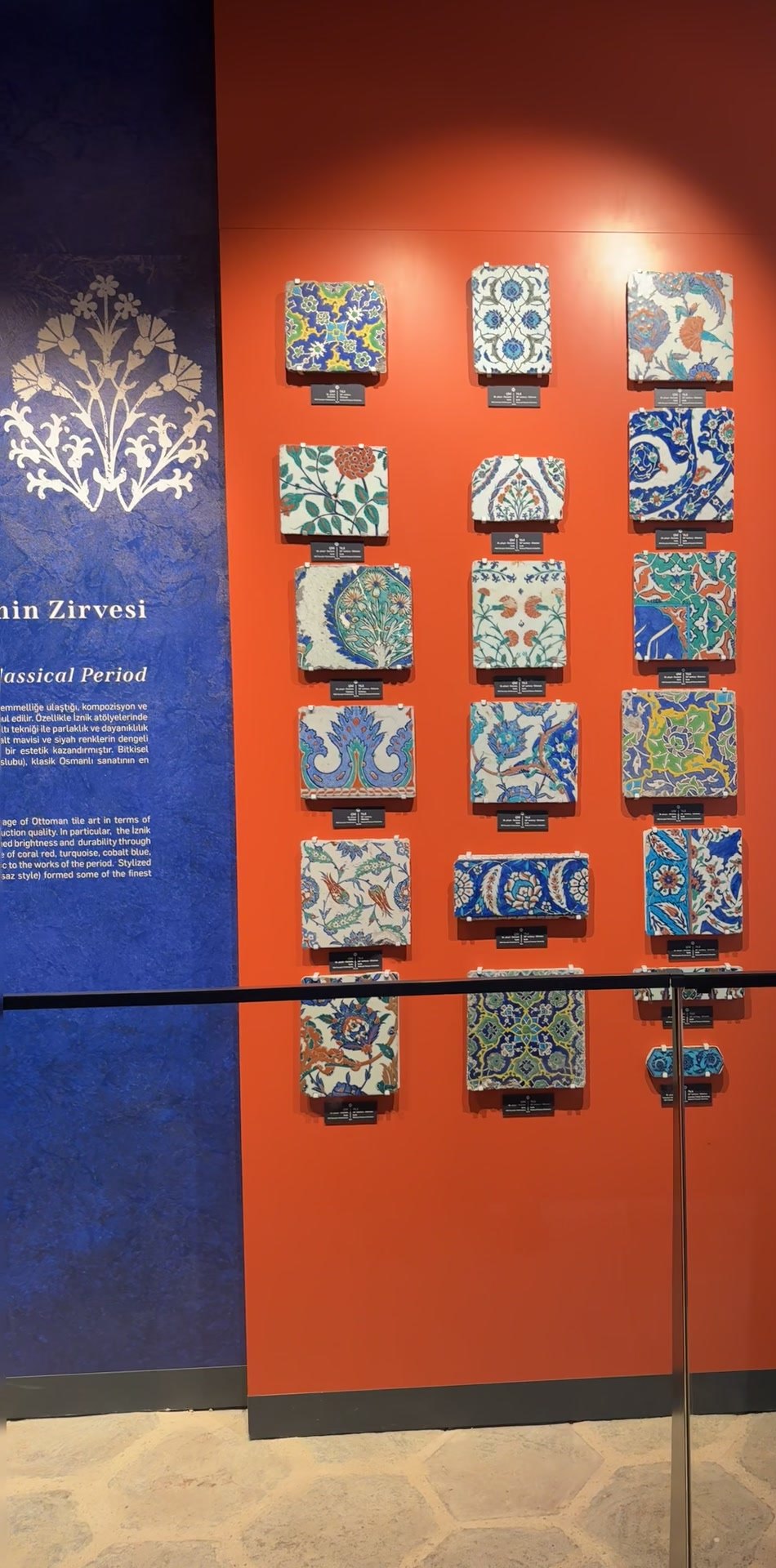 Display of single Iznik tiles on an orange panel against a blue wall in the Topkapı Harem