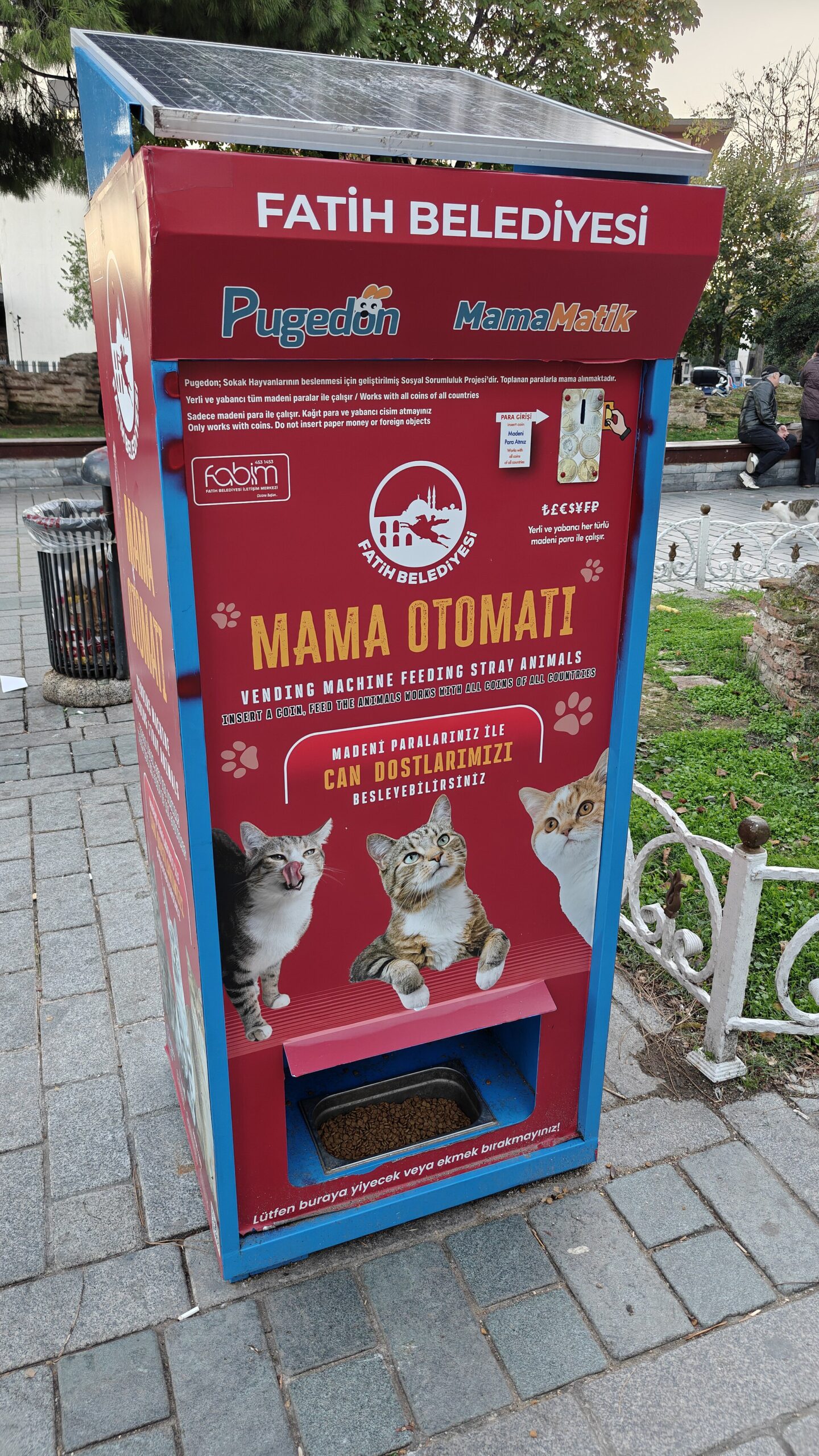 A red food dispenser for stray cats on an Istanbul pavement, marked as a Fatih municipality feeding machine