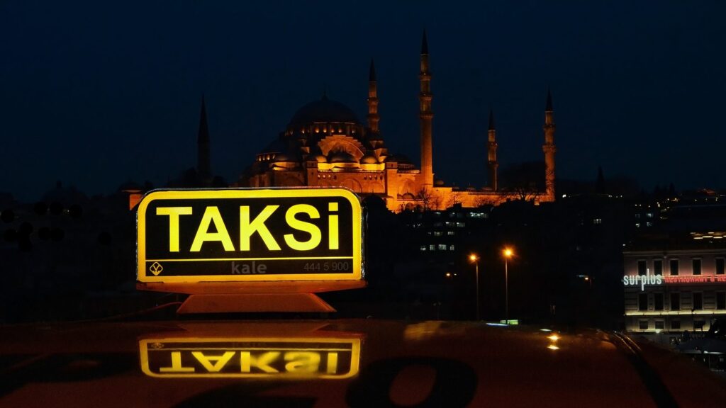 Illuminated TAKSİ roof sign on an Istanbul taxi at night, with the Süleymaniye Mosque lit up in the background
