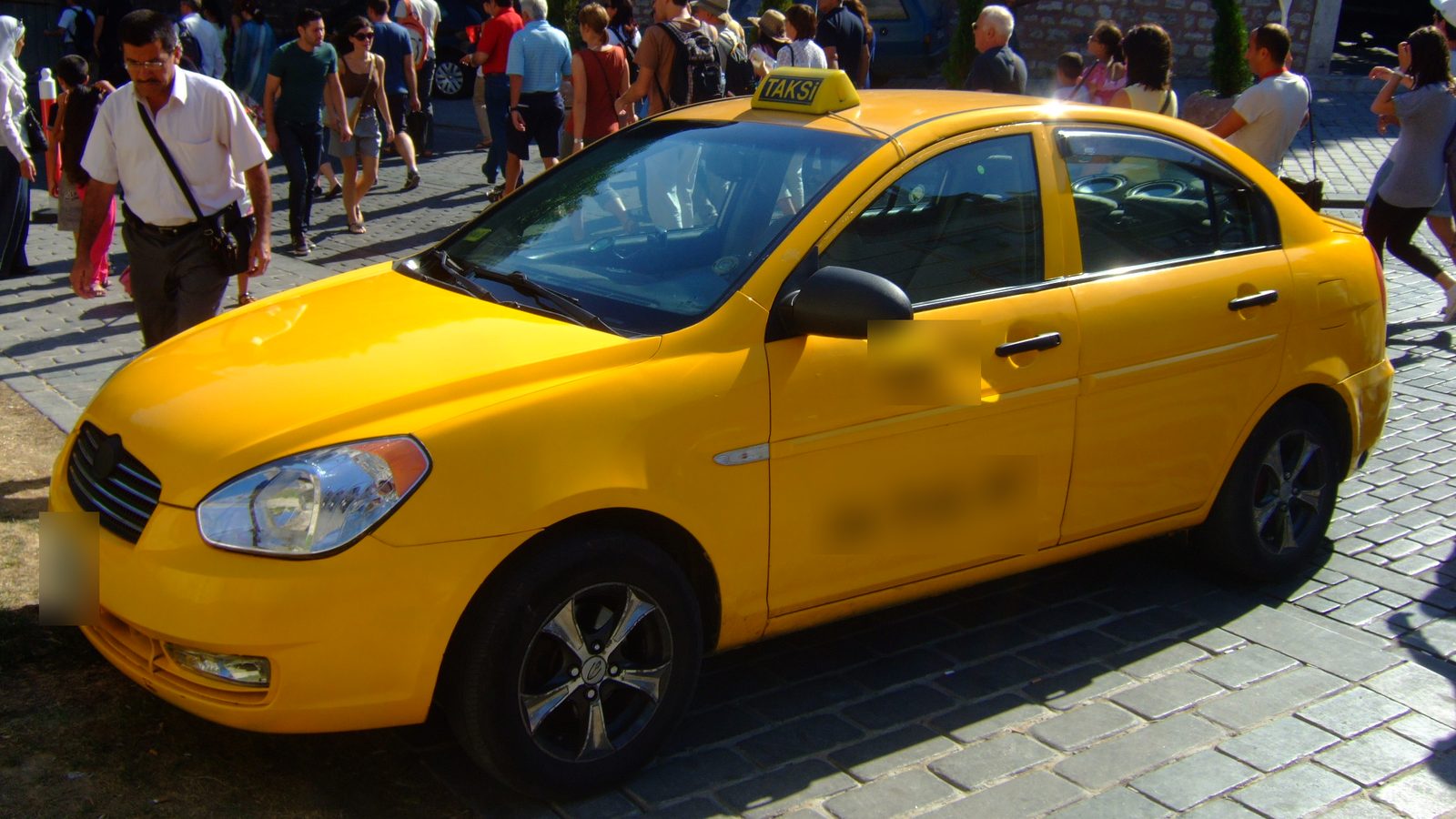 Yellow Istanbul taxi with a TAKSİ roof sign parked on a cobbled street in Sultanahmet, with pedestrians behind