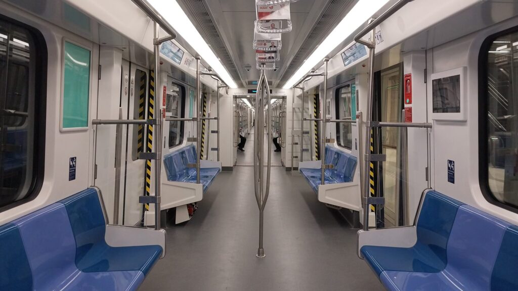 Inside an Istanbul metro train on the M11 line, with blue seats and open standing areas near the doors where large bags go