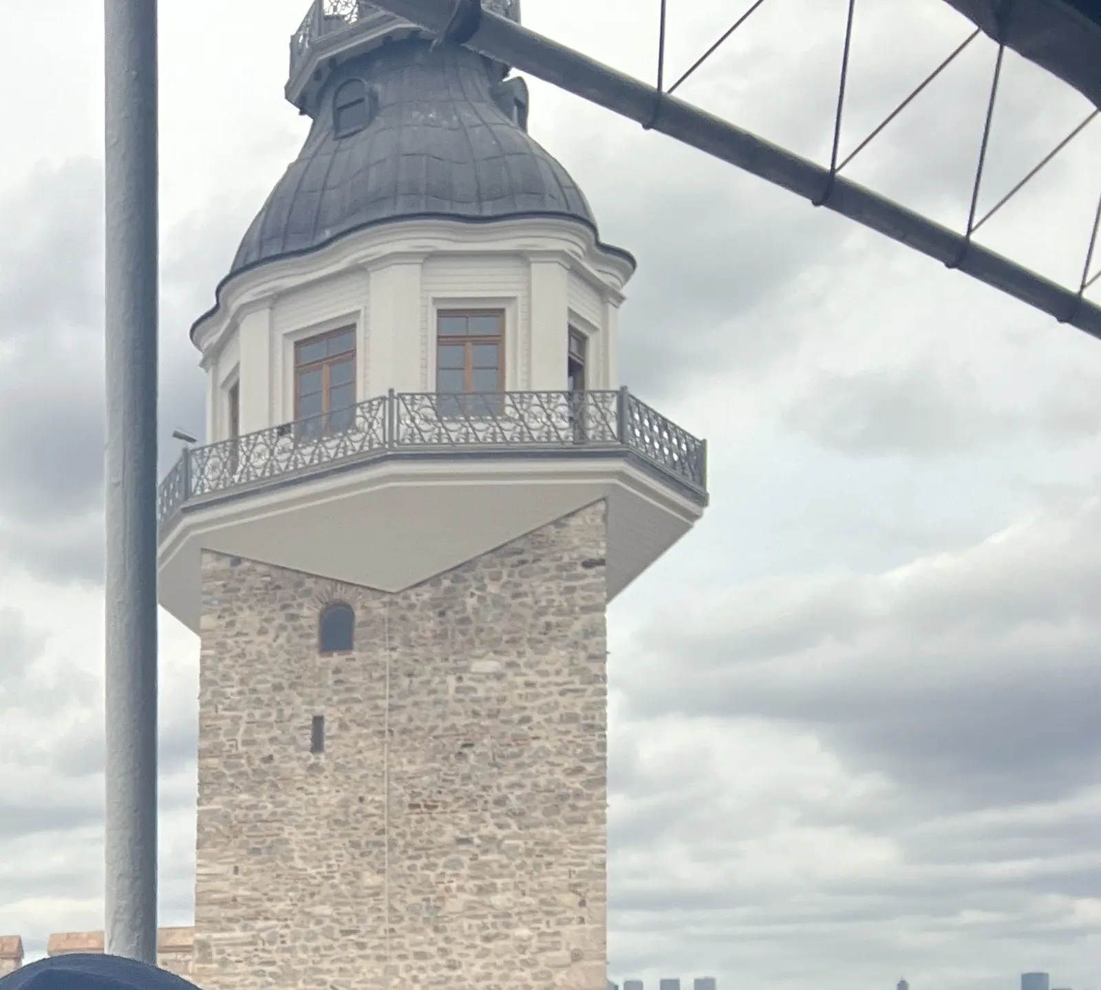 Close view of the tower's balcony, dome and flag pole against a cloudy sky