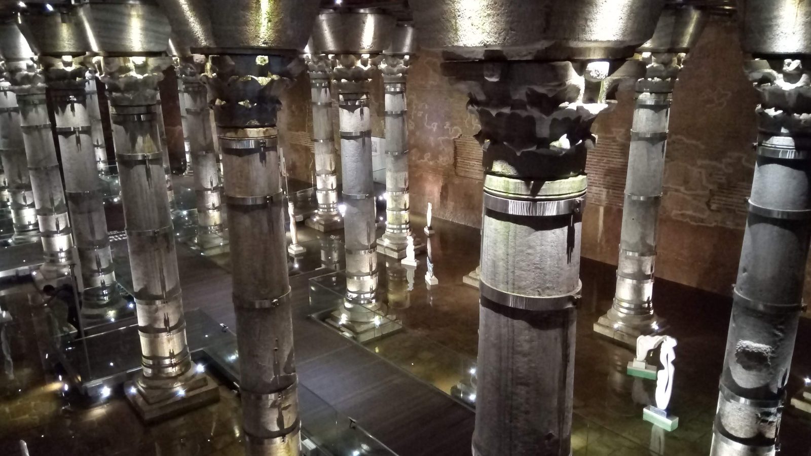 Lit stone columns and vaults inside the Şerefiye Cistern in Istanbul with a sculpture on display